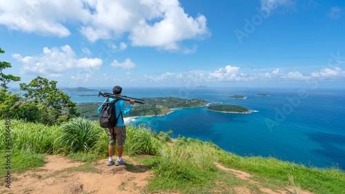 Travel man photographer standing on rock to see landscape view at Phahindum viewpoint popular landmark in Phuket Thailand Viewpoint to see promthep cape Naiharn beach and yanui beach Amazing view