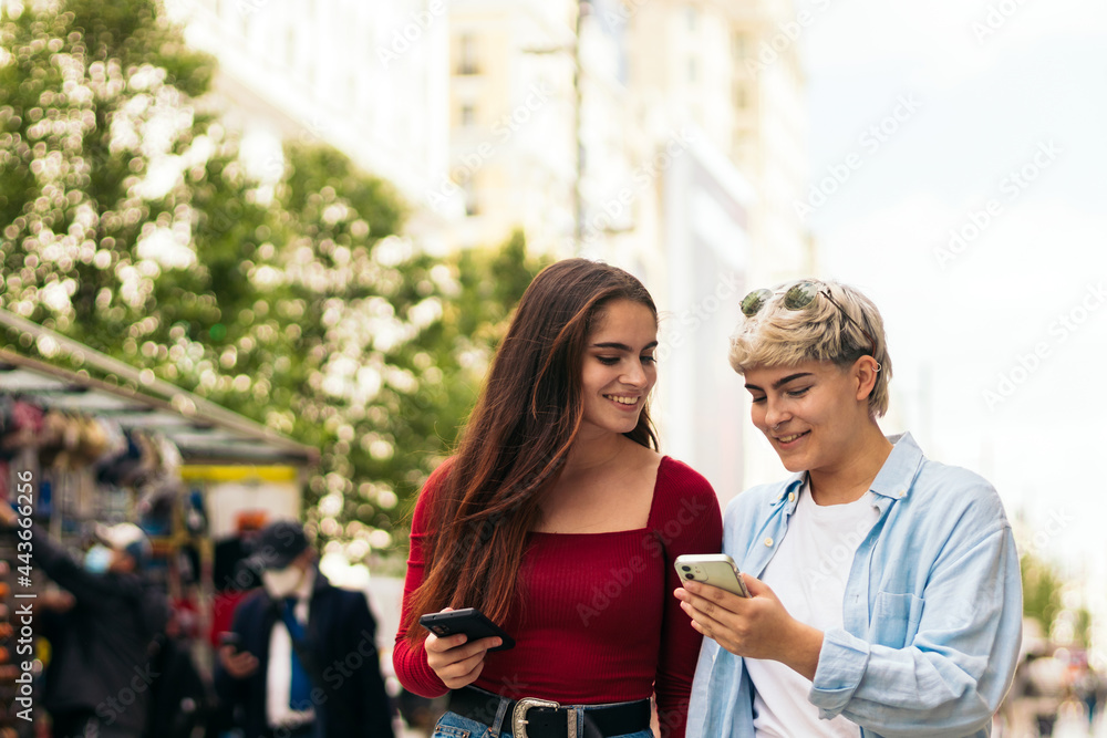 Two girls walking and watching something her mobiles Two girls walking and watching something her mobiles
