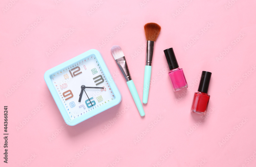 Makeup products and alarm clock on a pink background. Top view Makeup products and alarm clock on a pink background. Top view
