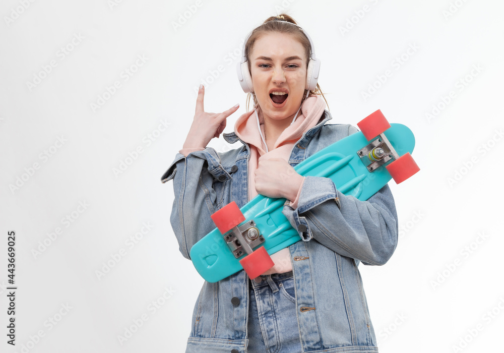 Young caucasian cheerful hipster woman in denim clothes with penny board and headphones listen music on white background Young caucasian cheerful hipster woman in denim clothes with penny board and headphones listen music on white background