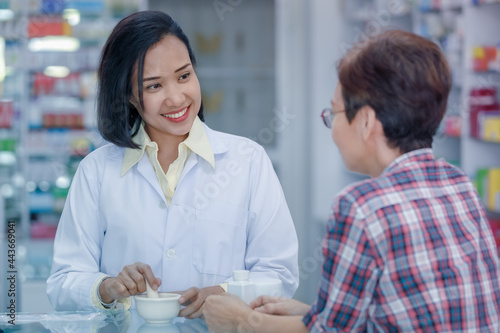 Asian female pharmacist or doctor explaining prescription medicine to patient female in a pharmacy.