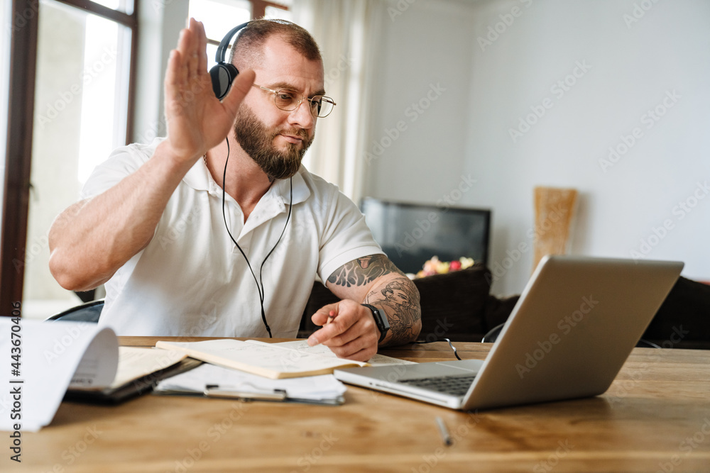 White man in headphones gesturing while working with laptop at home White man in headphones gesturing while working with laptop at home