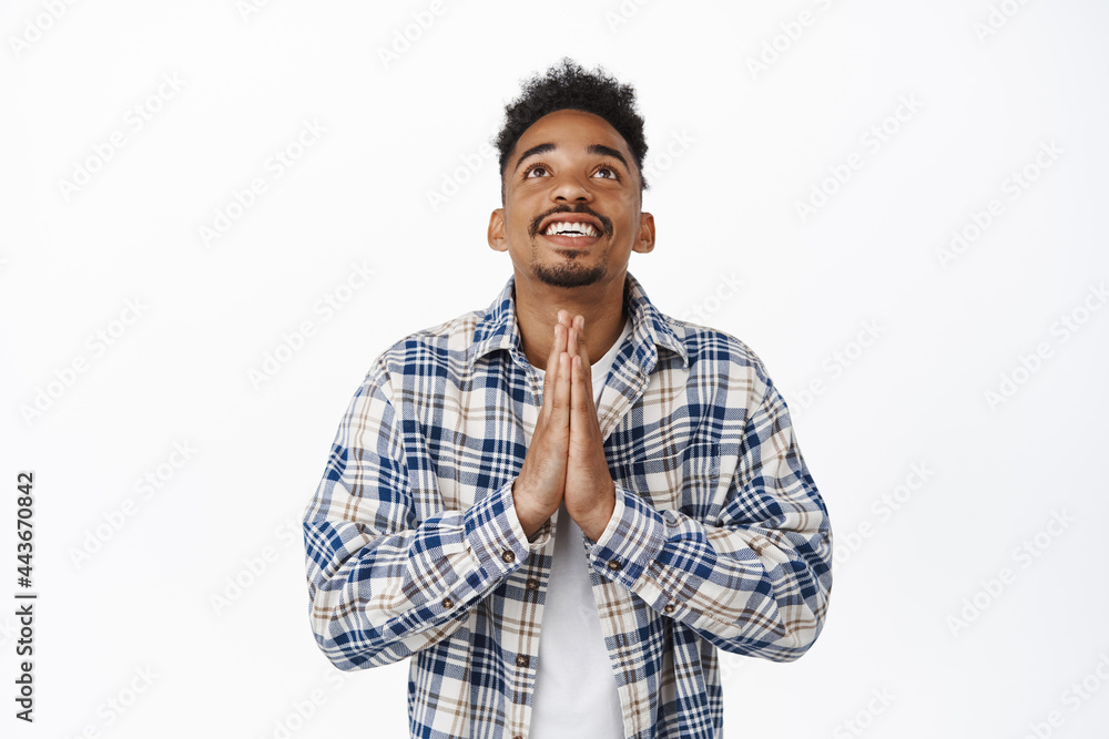 Hopeful african american man praying god, holding hands in begging supplication gesture, looking up in sky, beg Lord, standing in casual clothes against white background Hopeful african american man praying god, holding hands in begging supplication gesture, looking up in sky, beg Lord, standing in casual clothes against white background