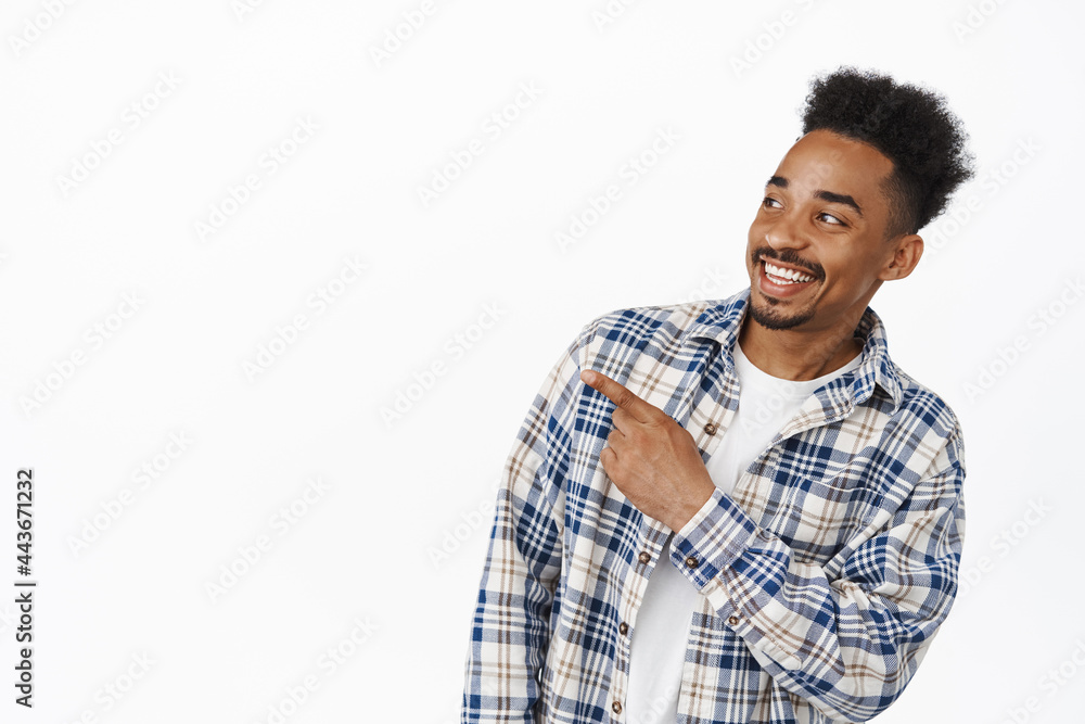 Portrait of handsome african american guy smiling happy, pointing and looking left at sale promo banner, showing advertisement, standing in casual clothes against white background Portrait of handsome african american guy smiling happy, pointing and looking left at sale promo banner, showing advertisement, standing in casual clothes against white background