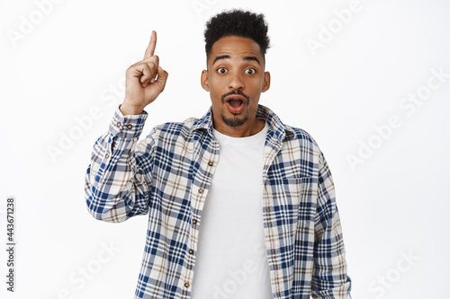 Portrait of handsome african american man pointing finger up, raising forefinger and showing price, sale banner, discount advertisement, standing against white background