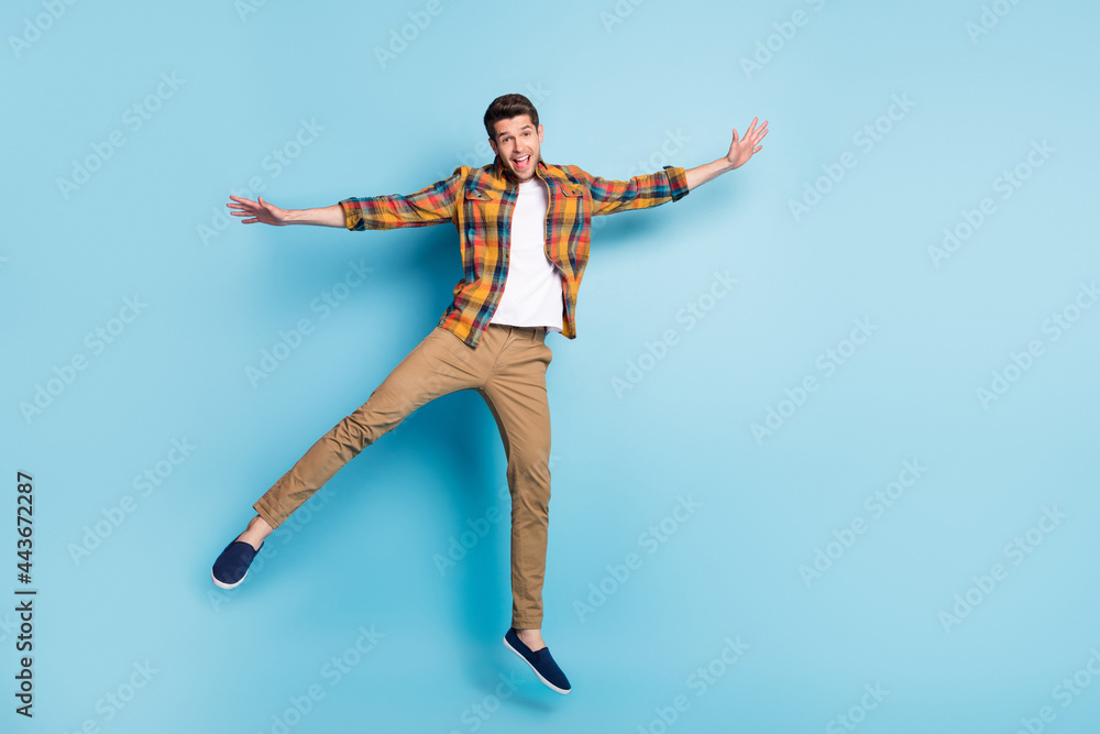 Photo of attractive carefree young gentleman wear checkered shirt jumping high smiling isolated blue color background
