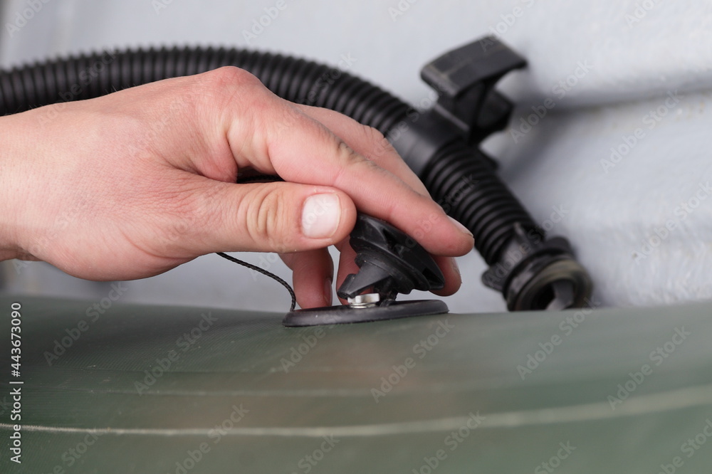 A man's hand opens the valve cover for blowing off an inflatable boat against the background of a pump hose