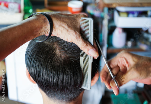 Closeup hands of hairsltylist and rear view of man having a hair cut by scissors and comb.