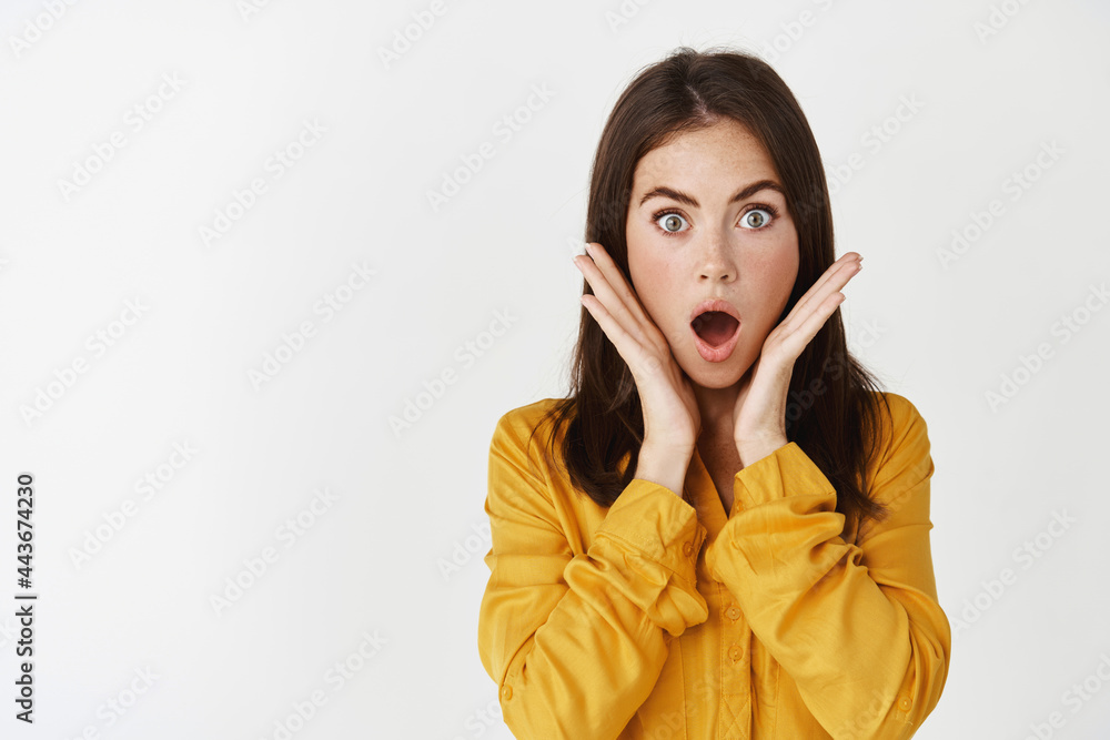 Close-up of shocked and speechless young woman gasping, staring at camera in complete disbelief, standing over white background Close-up of shocked and speechless young woman gasping, staring at camera in complete disbelief, standing over white background