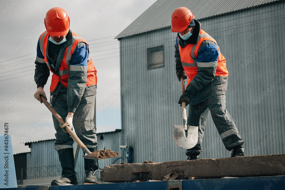 Hard Working Labourer Two workers in hard hats, work clothes and a medical mask work with ...