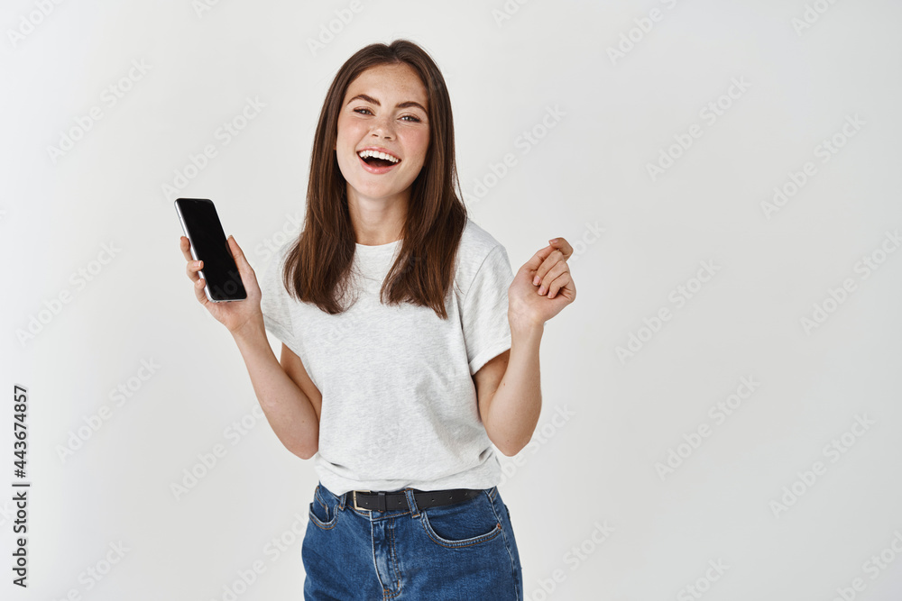 Cheerful brunette woman laughing and using mobile phone, standing happy with cellphone on white background Cheerful brunette woman laughing and using mobile phone, standing happy with cellphone on white background