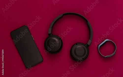 Modern gadgets. Smartphone with black stereo headphones and a smart bracelet on red background. Top view