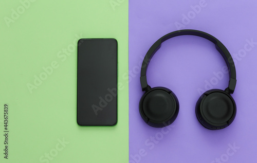 Smartphone with black stereo headphones on colored background. Top view