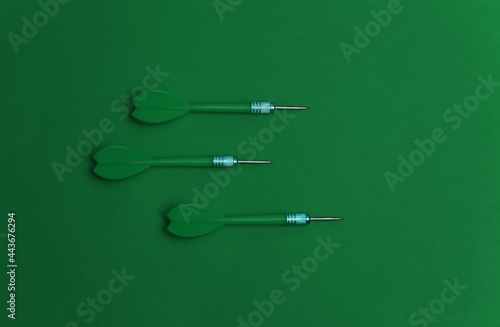 Three plastic darts with metal tip on green background. Top view. Flat lay