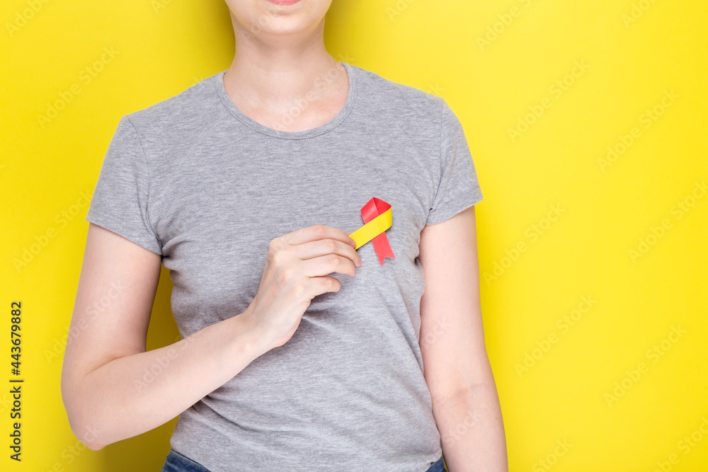 World Hepatitis Day concept. Girl in gray T-shirt holds in her hand awareness symbol red-yellow ribbon. Yellow background. Copy space World Hepatitis Day concept. Girl in gray T-shirt holds in her hand awareness symbol red-yellow ribbon. Yellow background. Copy space