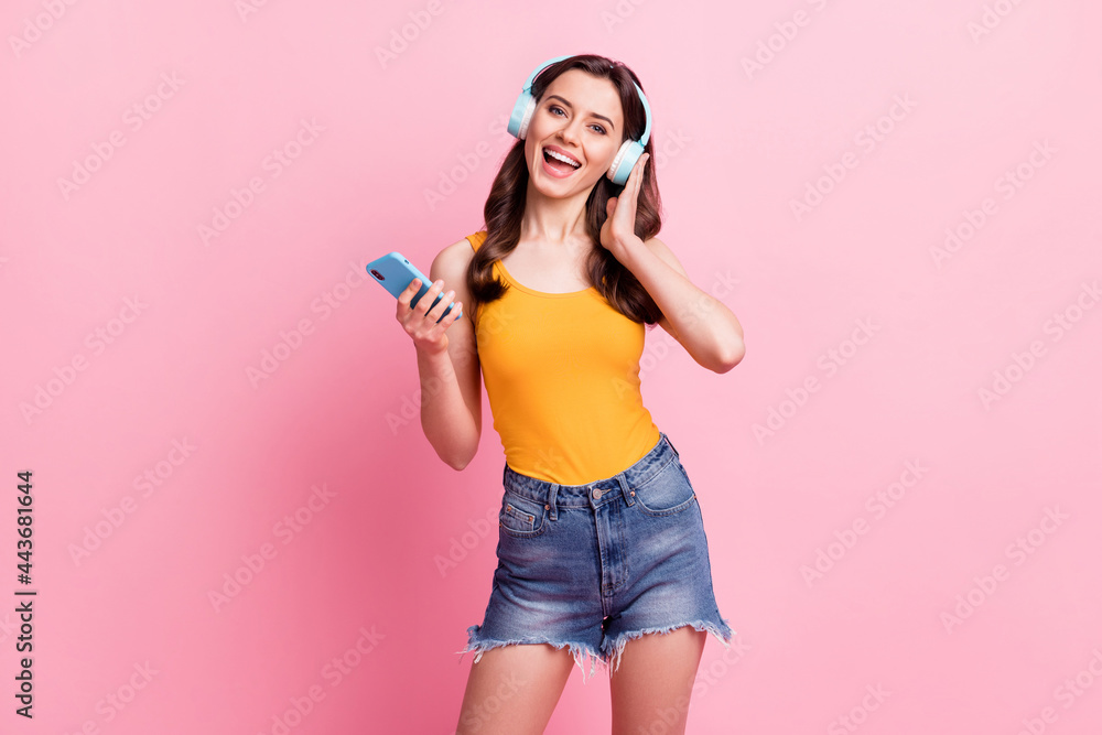 Photo of pretty cute young woman wear yellow singlet listening music holding modern gadget isolated pink color background Photo of pretty cute young woman wear yellow singlet listening music holding modern gadget isolated pink color background