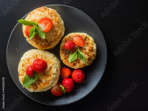 Cottage cheese pancakes with strawberries, mint and sour cream on a black background. syrniki. healthy dessert