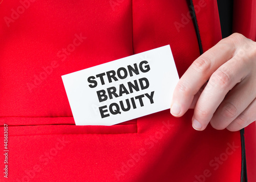 woman putting a card with text STRONG BRAND EQUITY in the pocket, hand close-up
