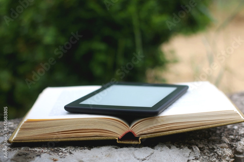 Open book and e-reader in a garden. Selective focus. photo