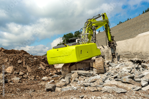 Photography A yellow excavator with hydraulic hammer chisels rocks