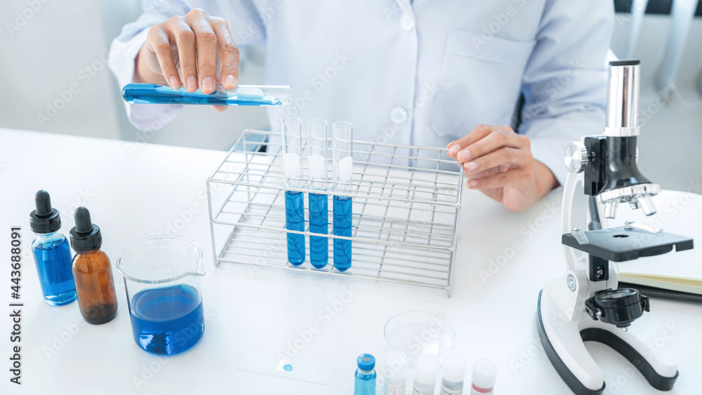 Scientist woman pouring blue liquid into test tube to making some experiments with microscope and substance Scientist woman pouring blue liquid into test tube to making some experiments with microscope and substance