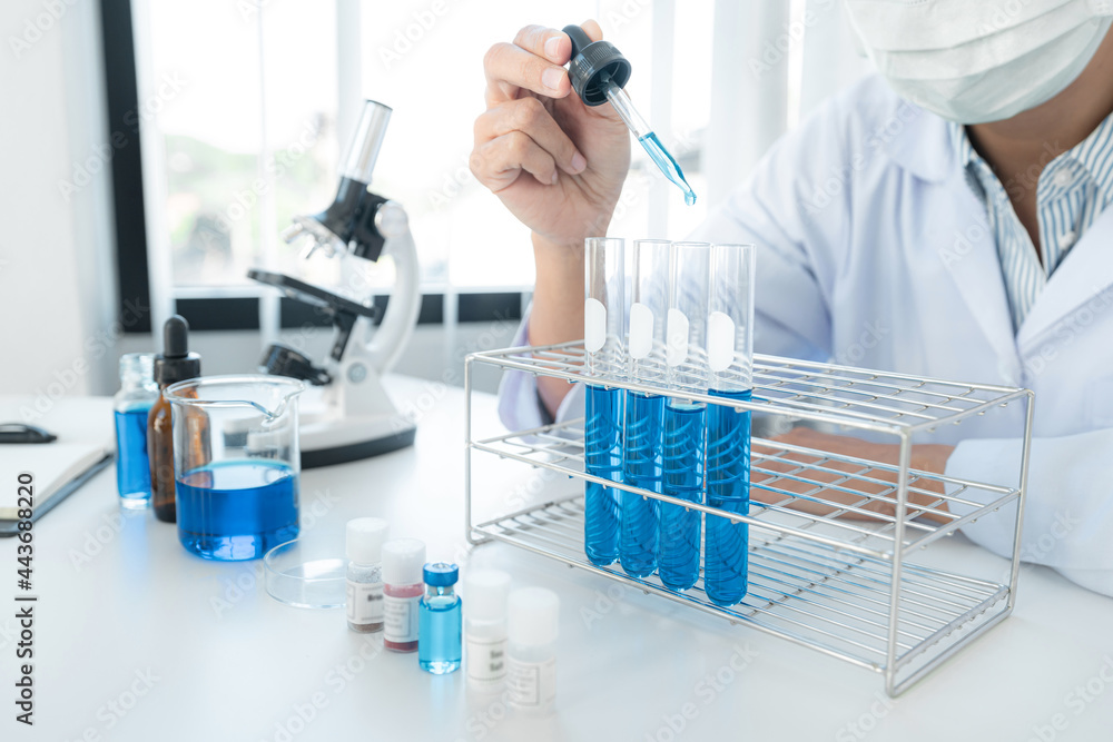 Scientist woman in medical face mask is using dropper to dropping solution into test tube and looking reaction Scientist woman in medical face mask is using dropper to dropping solution into test tube and looking reaction
