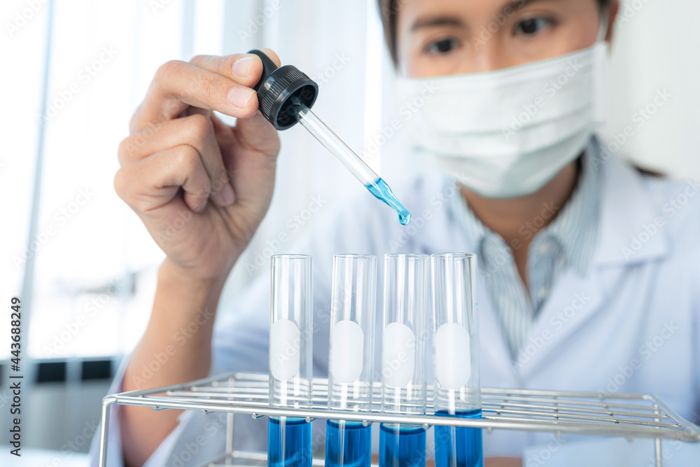Scientist woman in medical face mask is using dropper to dropping solution into test tube and looking reaction Scientist woman in medical face mask is using dropper to dropping solution into test tube and looking reaction