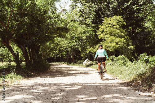 horizontal shot from behind of a female cyclist riding a bicycle running on a dirt road. mountain bike concept. photo