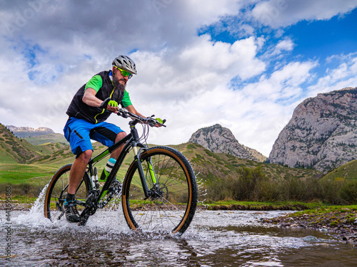 An athlete guy crosses a mountain river on a bicycle. Outdoor activities. Komirshi Gorge. Kazakhstan