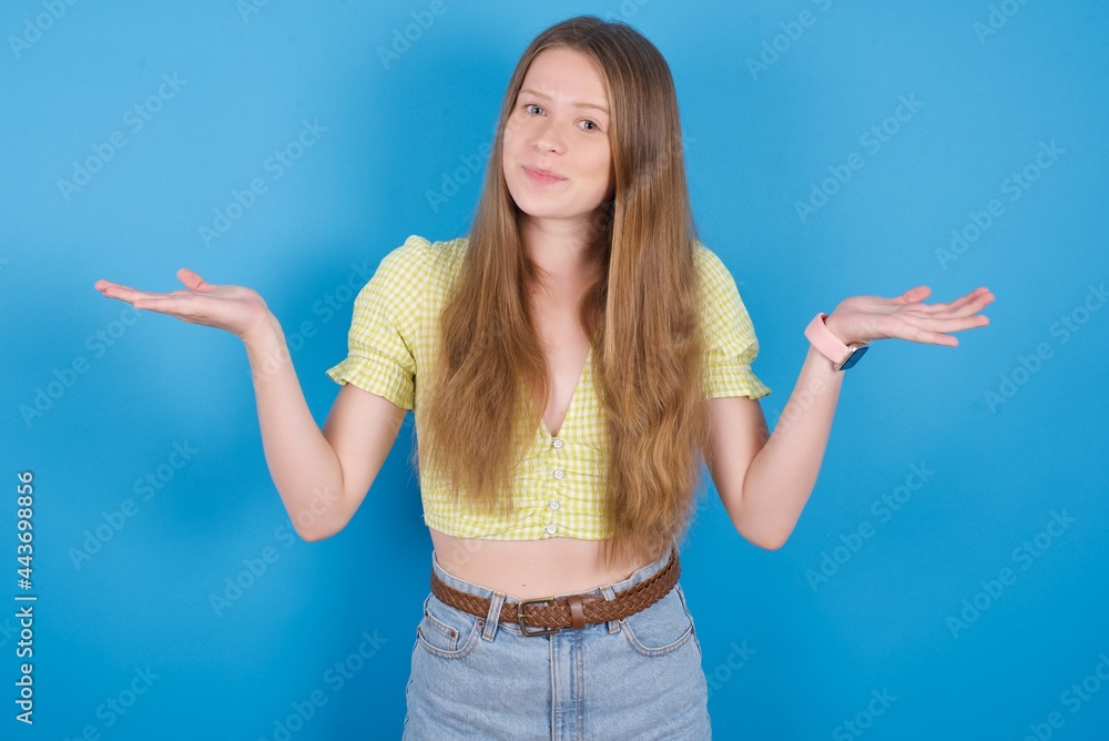 Maybe yes or no. Doubtful young beautiful blonde woman standing against blue background shrugs shoulders in bewilderment, tries to make decision puzzled what he wants. Hesitation and uncertainty. Maybe yes or no. Doubtful young beautiful blonde woman standing against blue background shrugs shoulders in bewilderment, tries to make decision puzzled what he wants. Hesitation and uncertainty.