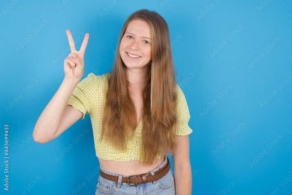young beautiful blonde woman standing against blue background showing and pointing up with fingers number two while smiling confident and happy. young beautiful blonde woman standing against blue background showing and pointing up with fingers number two while smiling confident and happy.