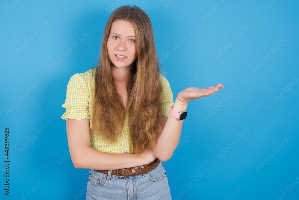 Studio shot of frustrated young beautiful blonde woman standing against blue background gesturing with raised palm, frowning, being displeased and confused with dumb question. Studio shot of frustrated young beautiful blonde woman standing against blue background gesturing with raised palm, frowning, being displeased and confused with dumb question.