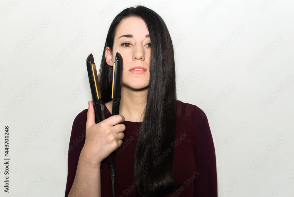 Pretty young woman with dark long hair holding a flat iron in one hand. Hair straightener Pretty young woman with dark long hair holding a flat iron in one hand. Hair straightener