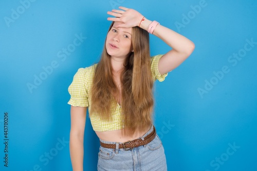 young beautiful blonde woman standing against blue background wiping forehead with hand making phew gesture, expressing relief feels happy that he prevented huge disaster. It was close enough photo