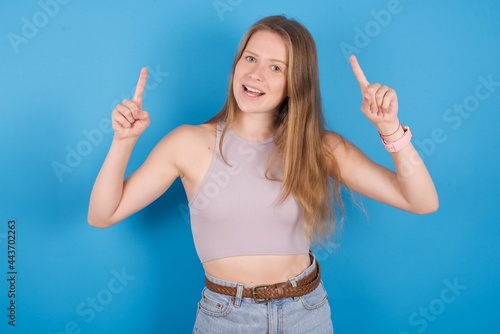 Cheerful young beautiful blonde woman standing against blue background demonstrating hairdo