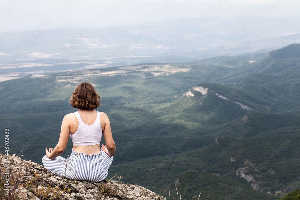 Young woman with short hair in a white T-shirt in nature in the mountains is engaged in yoga, general plan