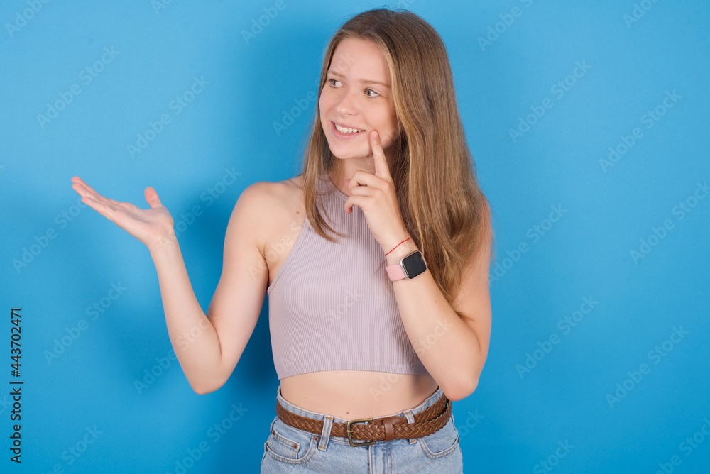 Positive young beautiful blonde woman standing against blue background advert promo touch finger teeth Positive young beautiful blonde woman standing against blue background advert promo touch finger teeth