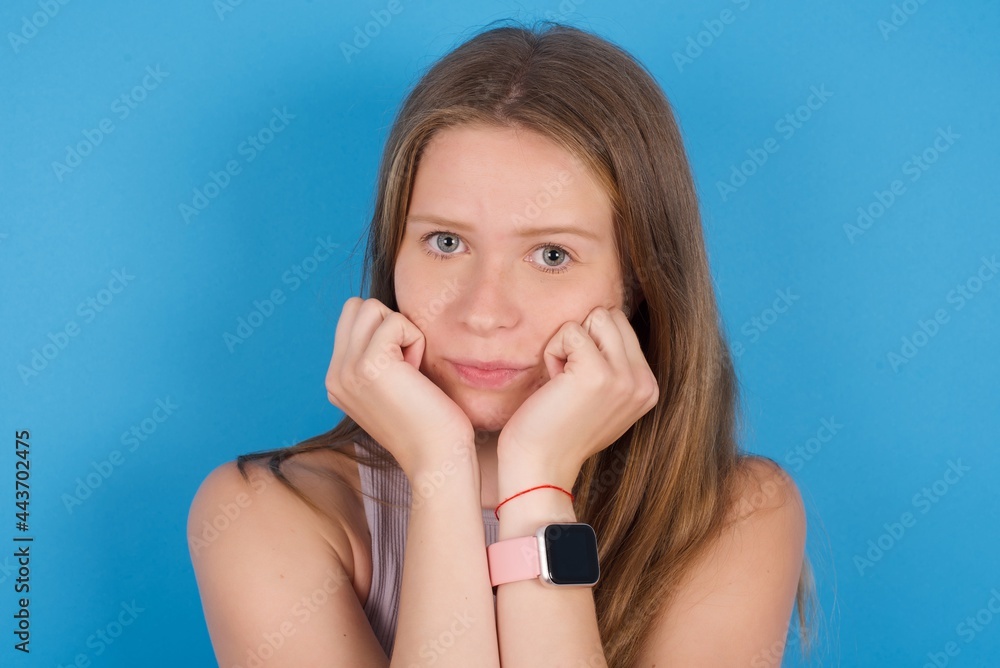 Portrait of sad young beautiful blonde woman standing against blue background hands face Portrait of sad young beautiful blonde woman standing against blue background hands face