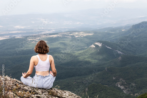 Young woman with short hair in a white T-shirt in nature in the mountains is engaged in yoga, general plan