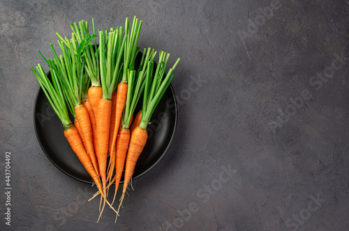 Raw carrots in a black plate on a brown background with space for copying.