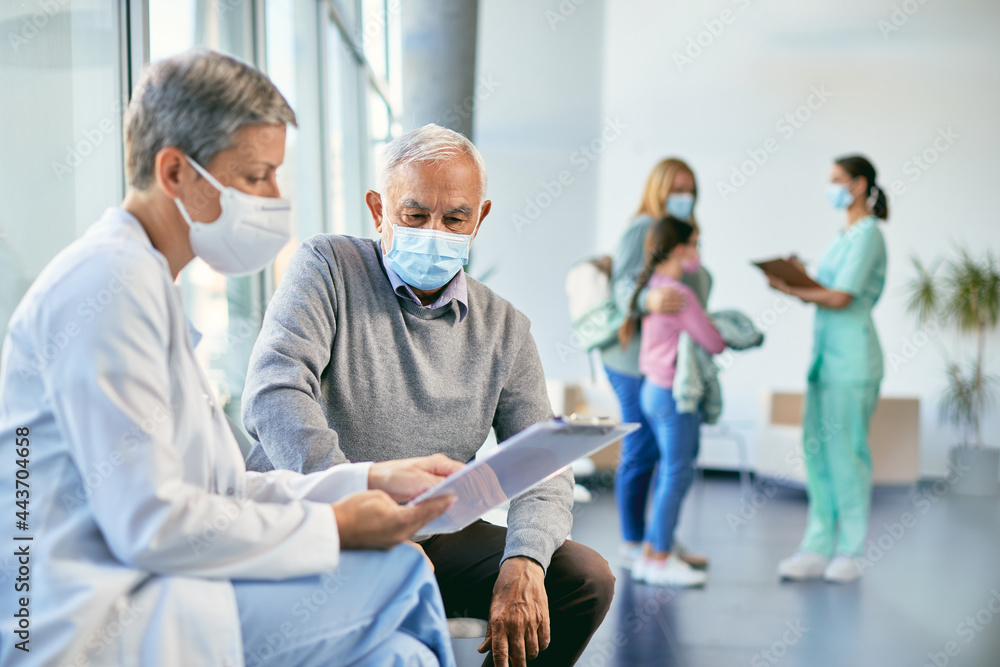 Senior man and his doctor wearing face masks while going through medical reports at the clinic. Senior man and his doctor wearing face masks while going through medical reports at the clinic.