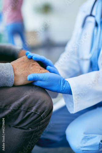 Close-up of caring doctor holding senior patient's hands at the hospital.