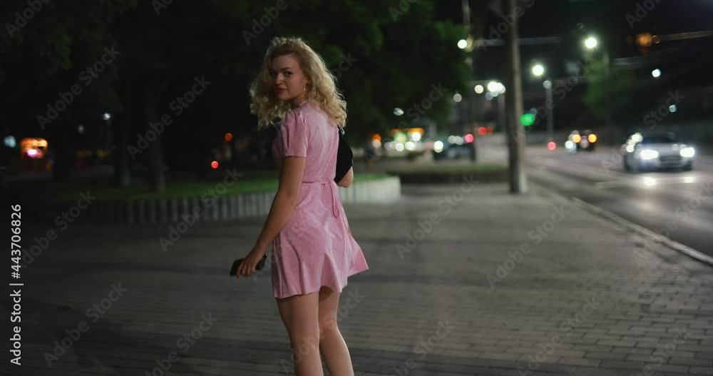 Sexy woman in dress walking at night city and turns face back Sexy woman in dress walking at night city and turns face back