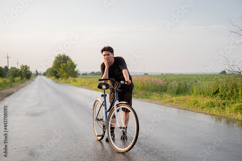 Young woman standing alone on road with bicycle looking at camera at countryside. Summer activity, healthy lifestyle, workout, sport, fitness. Person in nature. Riding bicycle. Having fun outdoors.