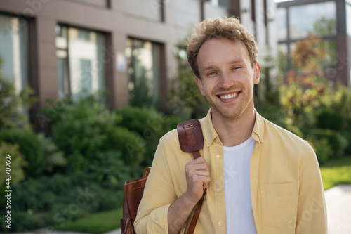 Smiling university student with backpack looking at camera standing in university campus. Portrait of young handsome  businessman wearing yellow shirt walking on the street. Successful business 