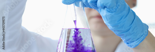 Woman scientist dripping purple liquid into flask with solvent closeup