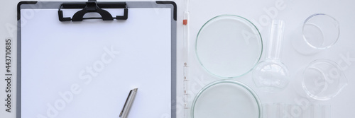 Clipboard with white sheet and pen lies on table next to flasks and chemical test tubes for experiments photo