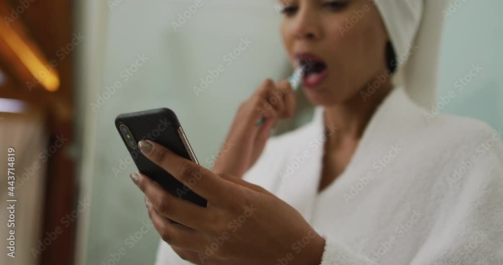 Mixed race woman brushing teeth using smartphone Mixed race woman brushing teeth using smartphone