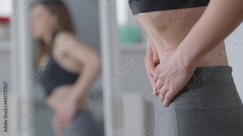 Side view of Caucasian young anorexic woman retacting belly with blurred reflection in mirror at background. Slim millennial trying lose more weight due to social pressure. Health care and dieting