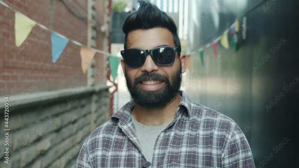 Slow motion portrait of cool Middle Eastern man standing outdoors wearing sun glasses smiling looking at camera. Stylish youth and urban background concept. Slow motion portrait of cool Middle Eastern man standing outdoors wearing sun glasses smiling looking at camera. Stylish youth and urban background concept.
